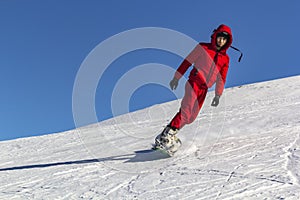 Snowboarder quickly rolls down the mountain in loose snow against a blue sky on a sunny day.