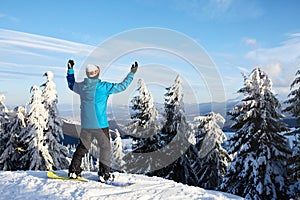 Snowboarder raised his arms and hands to the sky at ski resort. Man climbed a mountain top through forest for