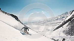 Snowboarder riding down the slope on deep fresh snow, rising wave of powder. Beautiful background of covered mountains