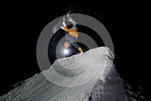 Snowboarder riding down the snowy mountain slope at the dark night