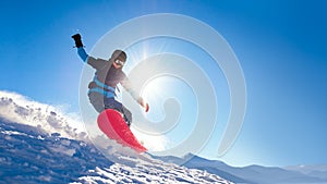 Snowboarder Riding Red Snowboard on the Slope in the Mountains in Bright Sun. Snowboarding and Winter Sports