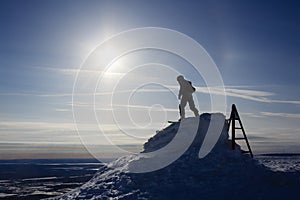 Snowboarder silhouette in sunlight on mountain top ready for descent