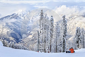 A snowboarder sitting on the snowy winter mountain slope of Sochi ski resort. Beautiful scenic landscape