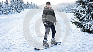 Snowboarder in ski glasses stands on a snowboard in the winter woods on the slopes