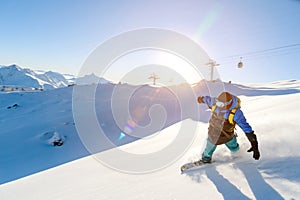 A snowboarder in a ski mask and a backpack is riding on a snow-covered slope leaving behind a snow powder against the