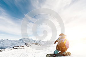 A snowboarder in a ski mask and a backpack is riding on a snow-covered slope leaving behind a snow powder against the