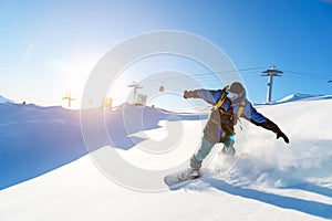 A snowboarder in a ski mask and a backpack is riding on a snow-covered slope leaving behind a snow powder against the