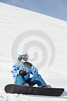 Snowboarder in ski suit sits on snowy hillside
