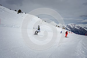 Snowboarder and Skier Descending Snowy Mountain Slope, Ski Resort Scene with Cloudy Sky