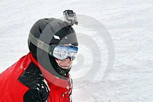 Snowboarder or skier portrait in sport goggles and protection helmet with mounted action camera and ski slope on background.