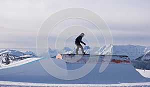 Snowboarder sliding a rail with mountains in the background