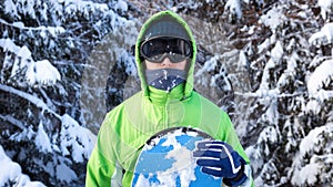 Snowboarder standing among the snow-capped fir trees in a ski mask
