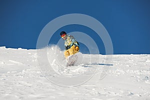 Snowboarder in stylish sportswear riding down the slope on sunny