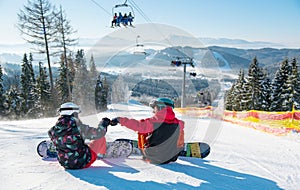 Snowboarders resting on top of ski slope under the lift