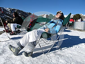 Snowboarders and skiers relax and sunbathe under the bright rays of the sun at the ski resort lying in sunbeds. Andorra, Andorra