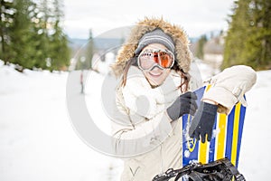 Snowboarding.Young beautiful woman with ski mask holding her snowboard at ski slope Young woman in ski resort