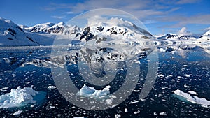 Snowcapped mountains in beautiful landscape, reflecting in blue water, ice flows, Lemaire Channel near Paradise Bay, Antarctica