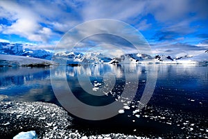 Snowcapped mountains in beautiful landscape, reflecting in blue water, ice flows, Lemaire Channel near Paradise Bay, Antarctica