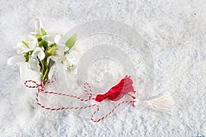 Snowdrops flowers with a red and white martenitsa on a snow background. Martisor and Baba Marta.