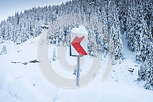 Snowed guide road sign of turn on a winter curved road through the mountains
