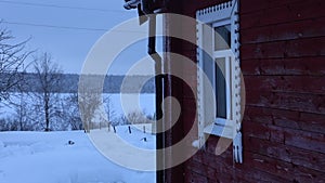 Snowfall against background of window of rural house and country landscape with lake and forest.