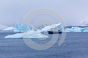 Snowfall and cruise liner among blue icebergs in Port Charcot, B