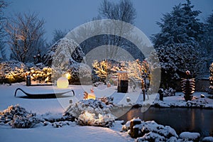 Snowfall in garden on winter evening. Beautiful illuminated private garden with illumined glass light objects