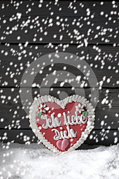 Snowfall with gingerbread heart on heap of snow against wooden background