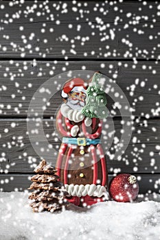 Snowfall with gingerbread santa claus christmas bulb chocolate christmas tree on heap of snow against wooden background