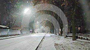 Snowfall landscape on city street at winter night. Two people walk on sidewalk