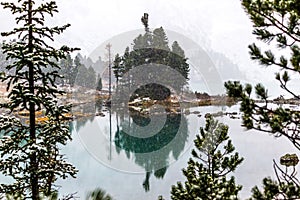 Snowfall on the mountain lake. Reflection of rocks and trees in the water surface.