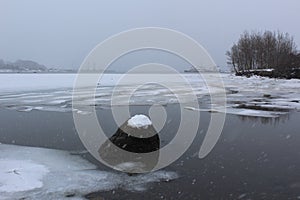 A snowfall on an overcast winter\'s day in Nova Scotia with a frozen bay and a port with ships in the distance