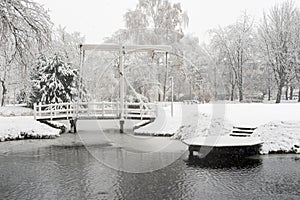 Snowfall in a park with a bridge and a pond