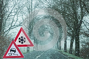 Snowfall with warning signs for snowfall and slipperiness