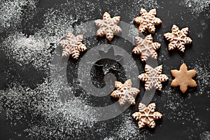 Snowflake gingerbread cookie decorated with sugar icing, cookie cutter on black table background with flour, flat lay