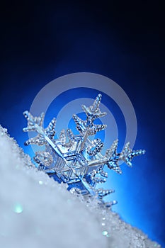 Snowflake on glittering white snow with sparkling blue background