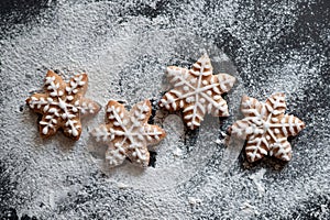 Snowflake shape gingerbread cookie decorated with sugar icing, on black table background with flour. Traditional