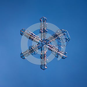 Snowflake on smooth gradient background. Macro photo of real snow crystal on glass surface. This is small snowflake with