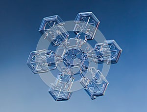 Snowflake on smooth gradient background. Macro photo of real snow crystal on glass surface. This is small snowflake with