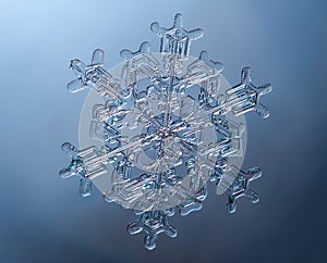 Snowflake on smooth gradient background. Macro photo of real snow crystal on glass surface. This is small snowflake with