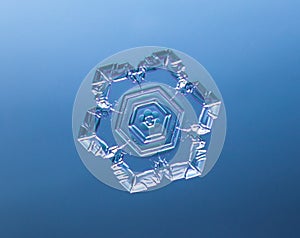 Snowflake on smooth gradient background. Macro photo of real snow crystal on glass surface. This is small snowflake with