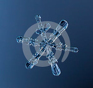 Snowflake on smooth gradient background. Macro photo of real snow crystal on glass surface. This is small snowflake with