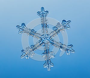 Snowflake on smooth gradient background. Macro photo of real snow crystal on glass surface. This is small snowflake with