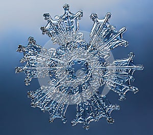 Snowflake on smooth gradient background. Macro photo of real snow crystal on glass surface. This is small snowflake with