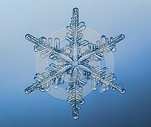 Snowflake on smooth gradient background. Macro photo of real snow crystal on glass surface. This is small snowflake with