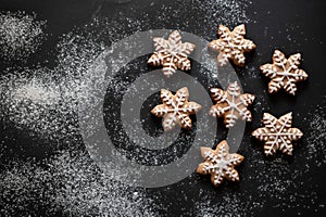 Snowflake sugar gingerbread cookie with frosting decoration, on black table background with flour, flat lay, copy space