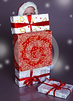 Snowing Christmas photo of funny little boy hoding behind the gift-box