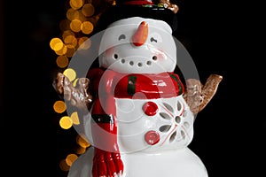 Snowman ceramic figurine decoration with Christmas tree lights bokeh.