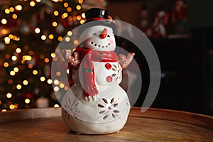 Snowman ceramic figurine decoration with Christmas tree lights bokeh.