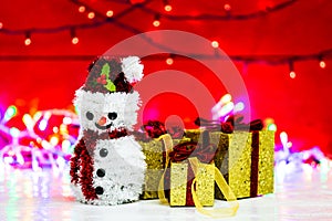 Snowman Christmas figurine near glittery gifts isolated on blurred background of lights. Christmas decorations isolated